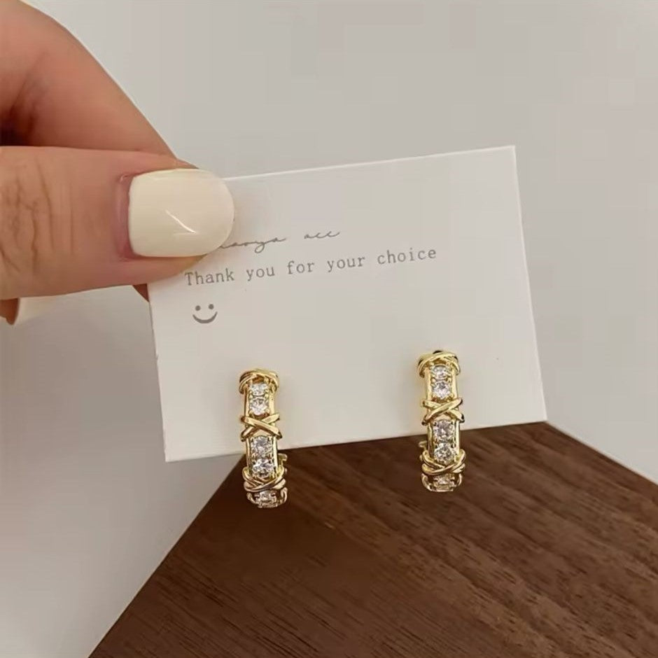 A pair of gold-tone hoop earrings adorned with sparkling crystals and featuring a unique 'X' detailing.