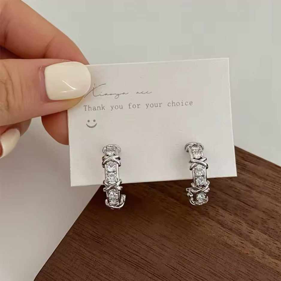 A pair of silver-tone hoop earrings adorned with sparkling crystals and featuring a unique 'X' detailing.