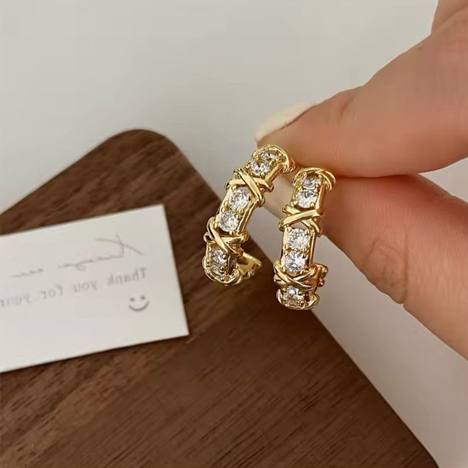 A pair of gold-tone hoop earrings adorned with sparkling crystals and featuring a unique 'X' detailing.