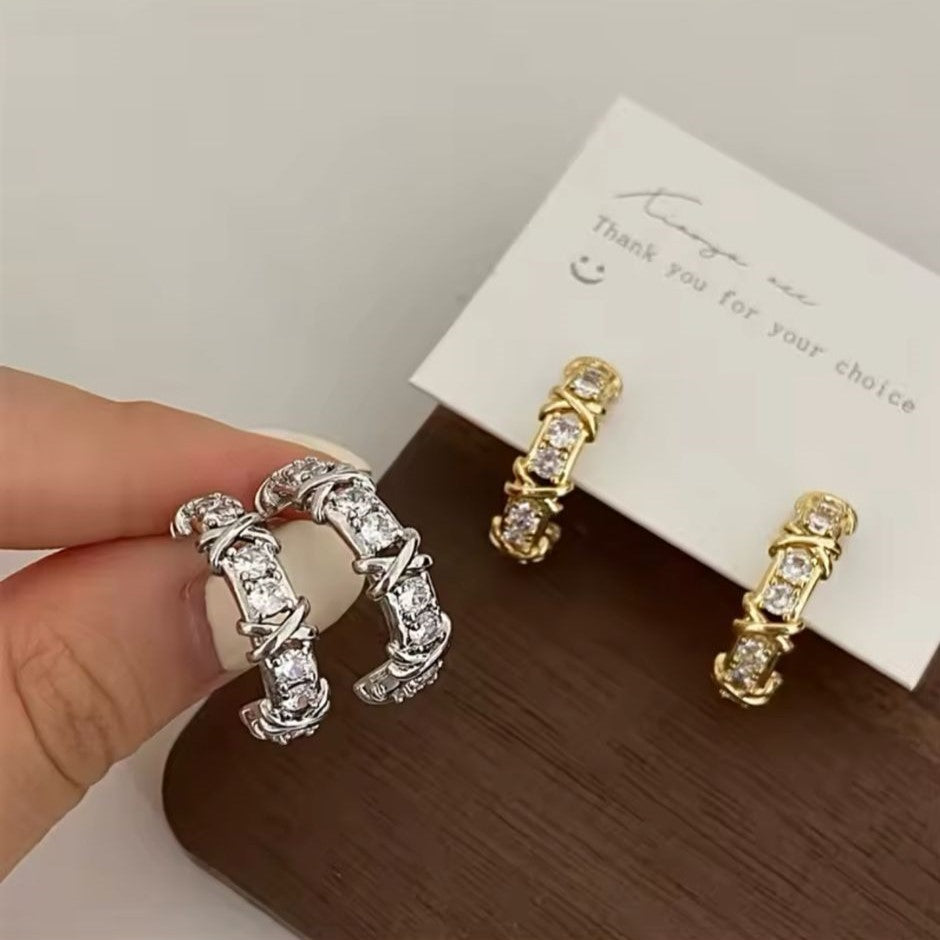 Pairs of silver and gold-tone hoop earrings adorned with sparkling crystals and featuring a unique 'X' detailing.