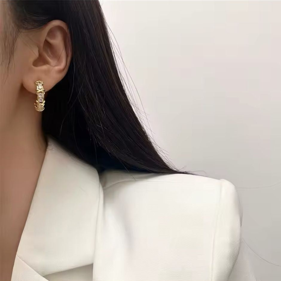 A gold-tone hoop earring adorned with sparkling crystals and featuring a unique 'X' detailing.
