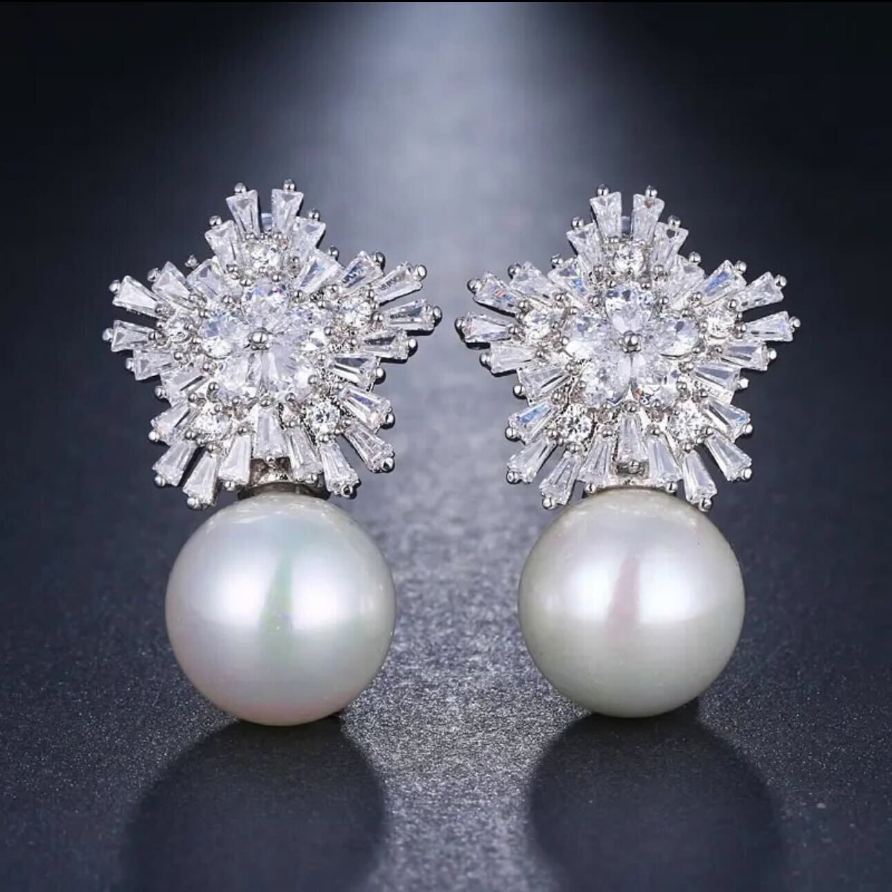 A pair of pearl earrings with raised texture and bullet-clutch back, likely silver or white gold, displayed against a dark background.