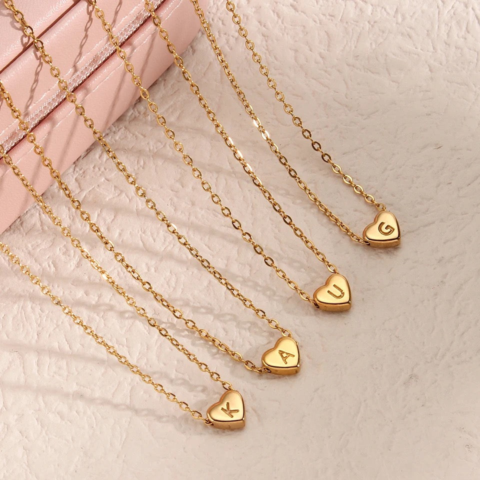 Four gold-colored heart initial necklaces with the letter 'K', 'A', 'U' and 'G' on a chain.