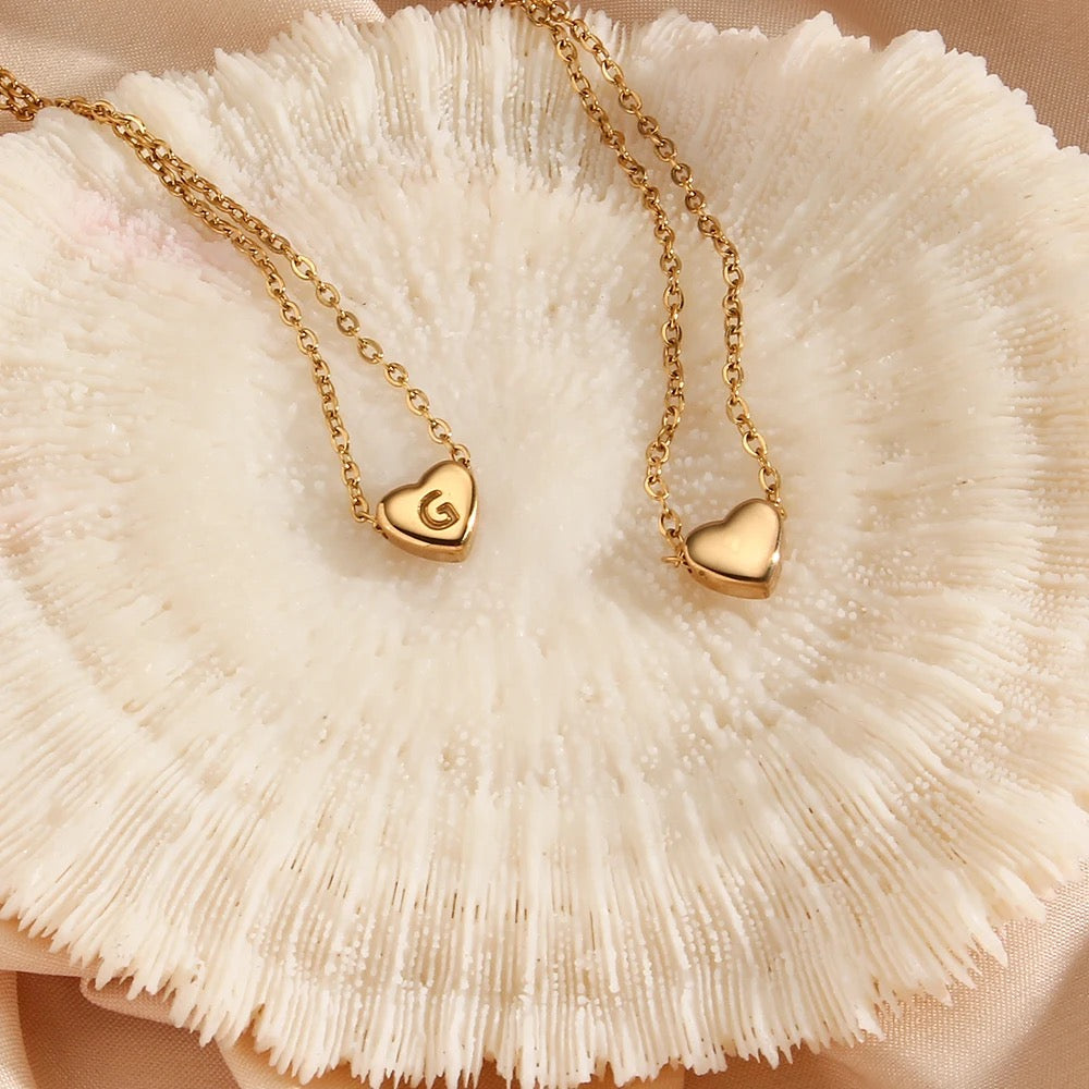 Two gold-colored heart initial necklaces with the letter 'G' on a chain.