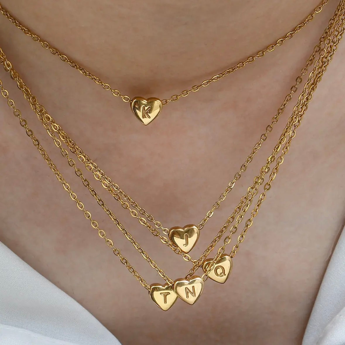 A collection of gold-colored heart initial necklaces with different initial letters on a chain.