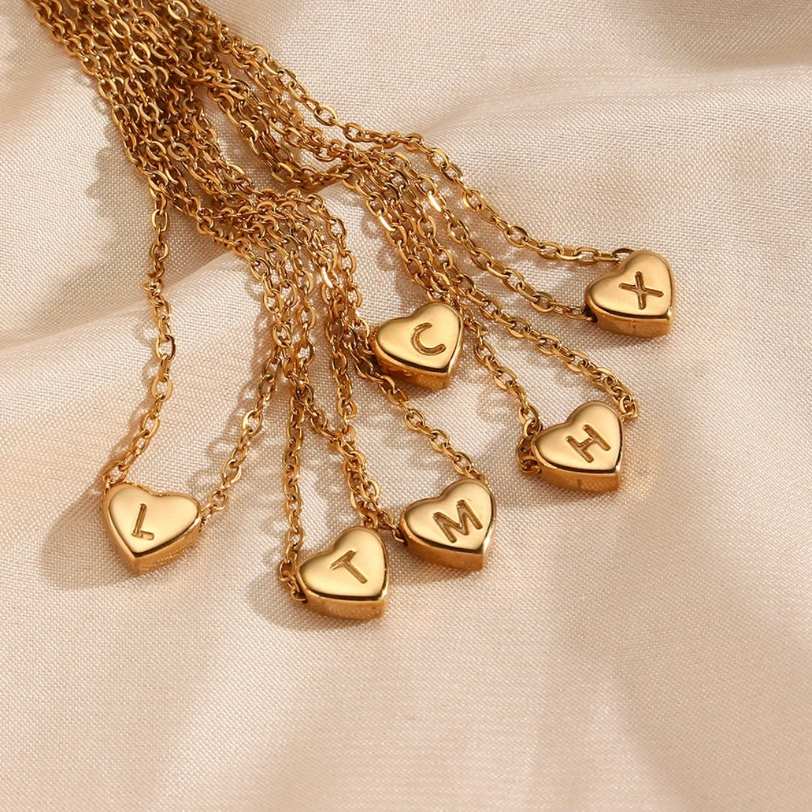 A collection of gold-colored heart initial necklaces with different initial letters on a chain.