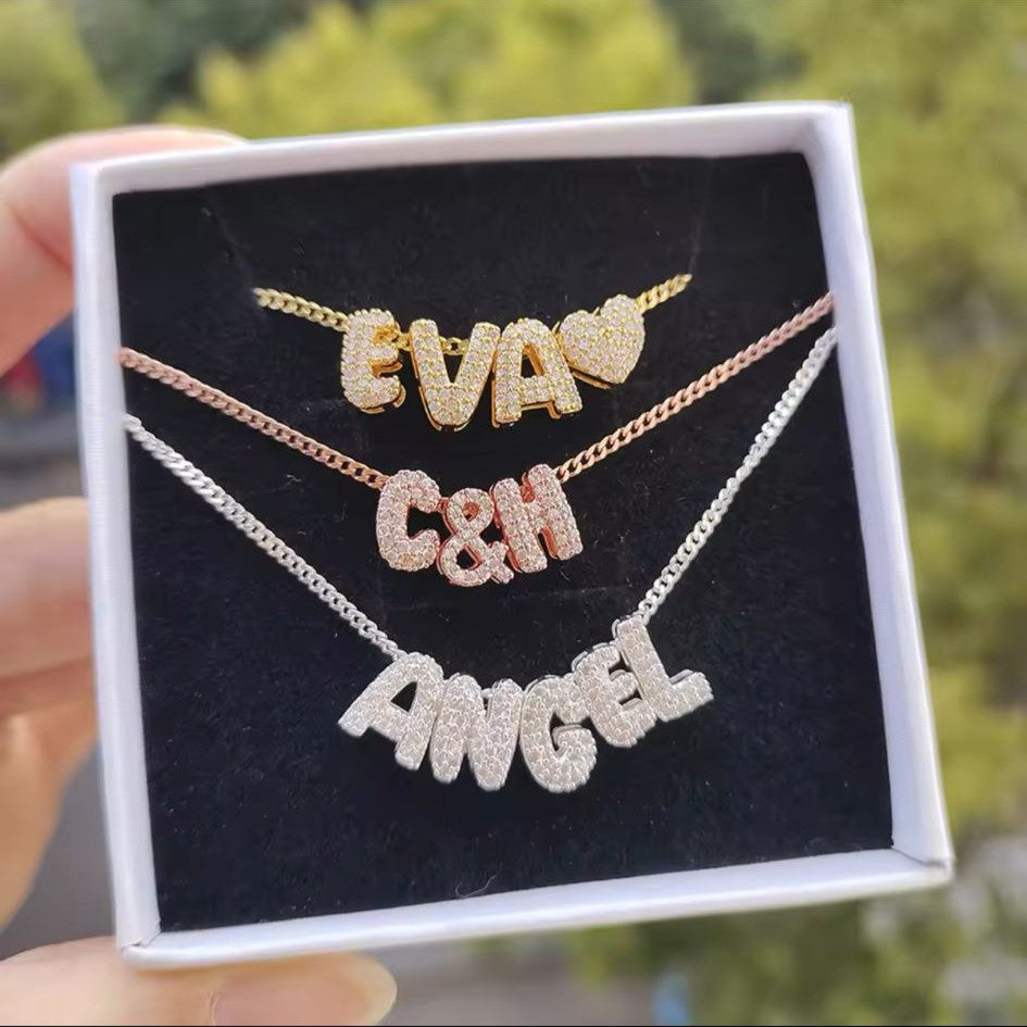 Three personalized bubble letter charm necklaces in gold, silver and bronze tone, with necklace displaying charms, displayed on a box.