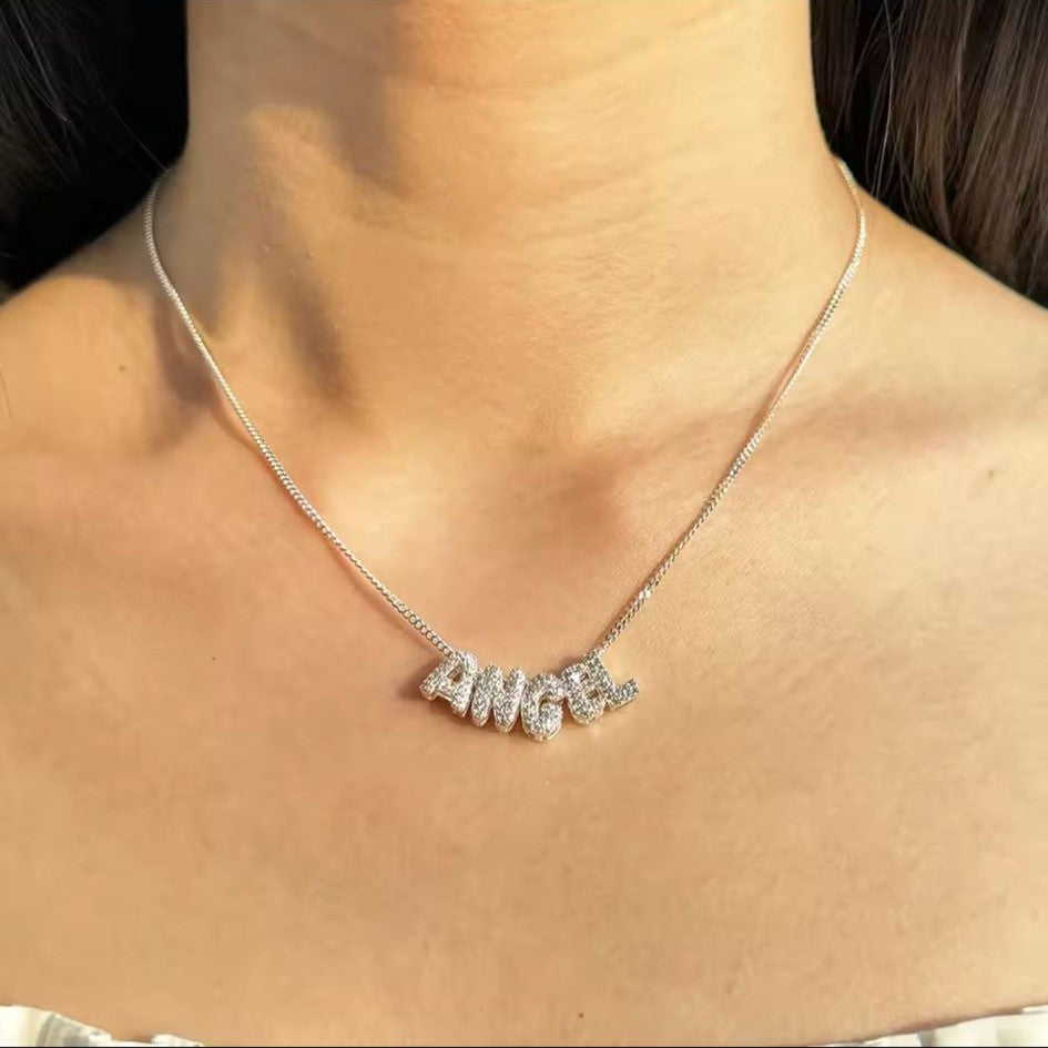 A personalized bubble letter charm necklace in silver tone, with necklace displaying charms, displayed on a women's neck.