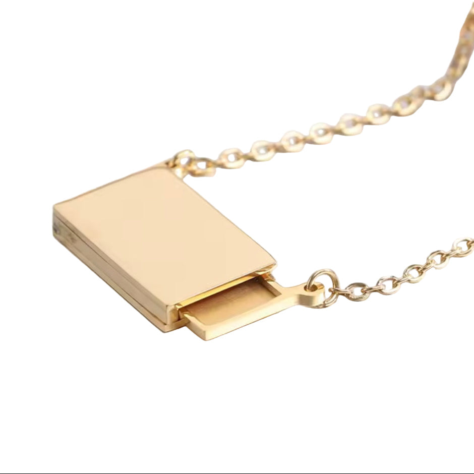 Gold necklace with a rectangular pendant on a light gray background