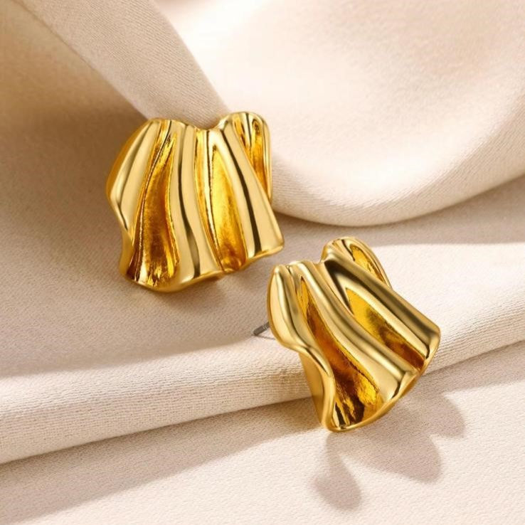 A pair of gold-colored, wave-shaped metal earrings resting on a beige surface.