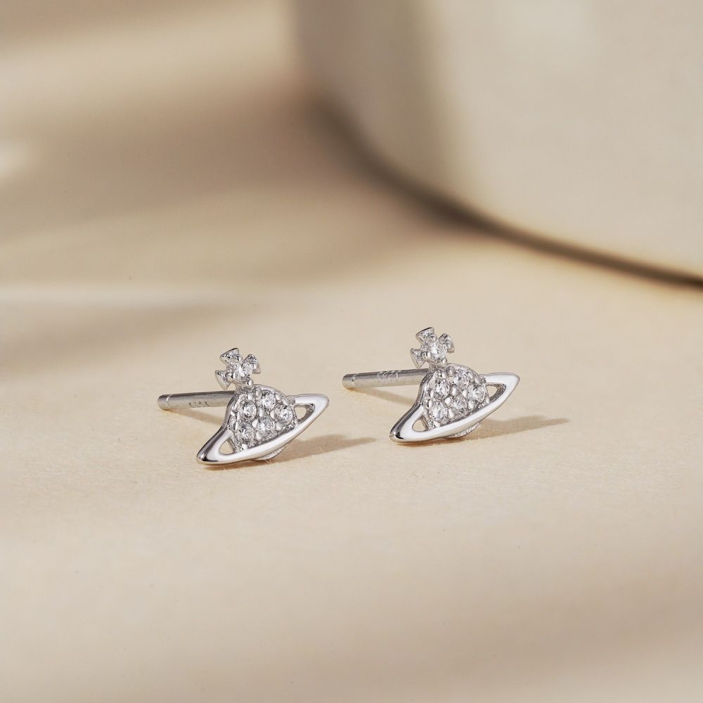 A pair of silver-colored stud earrings featuring a cosmic orbit design with sparkling stones, displayed against a light background.