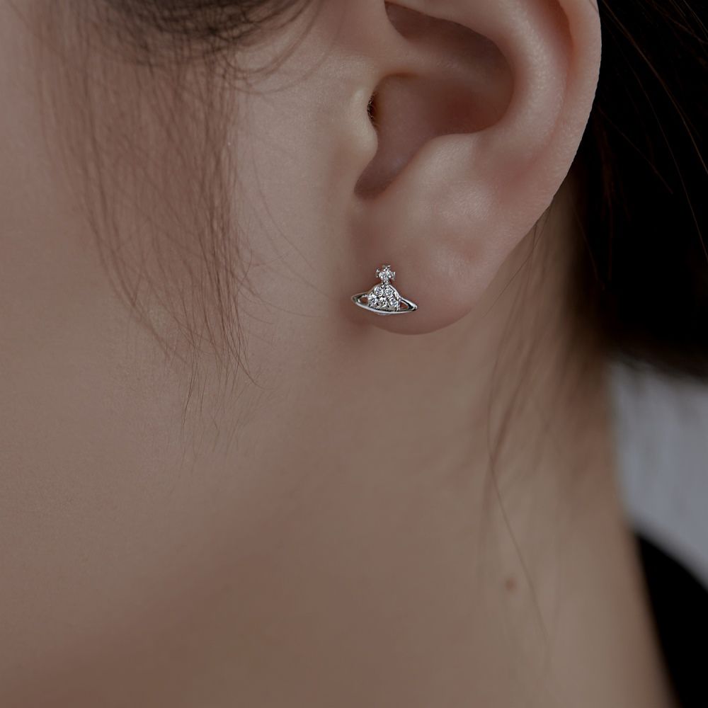 A silver-colored stud earring featuring a cosmic orbit design with sparkling stones, displayed on women's ear.
