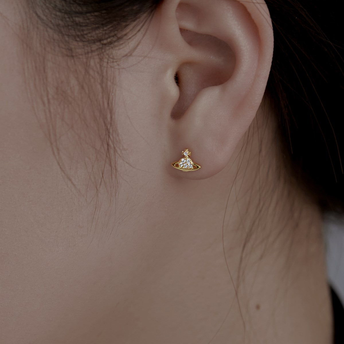 A gold-colored stud earring featuring a cosmic orbit design with sparkling stones, displayed as women wearing it.