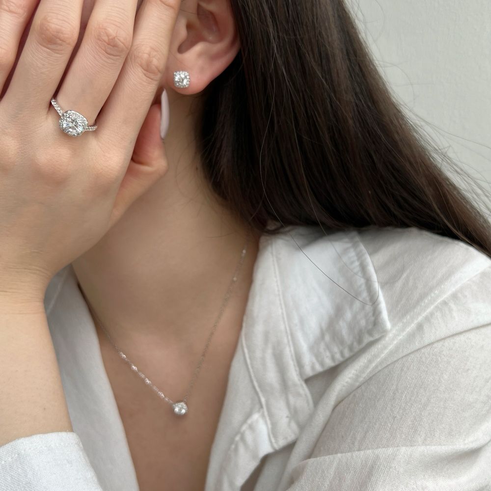 A sterling silver pendant necklace with a central sparkling stone surrounded by smaller stones, attached to a rhodium-plated chain along with an earring and a ring.