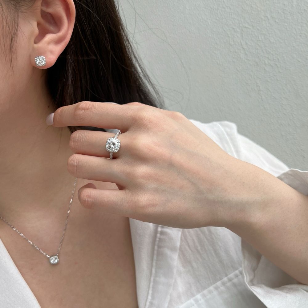 A sterling silver pendant necklace with a central sparkling stone surrounded by smaller stones, attached to a rhodium-plated chain along with an earring and a ring.
