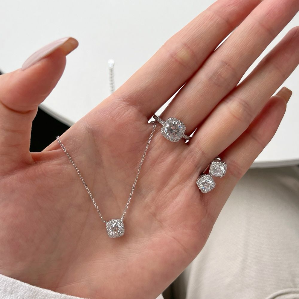 A sterling silver pendant necklace with a central sparkling stone surrounded by smaller stones, attached to a rhodium-plated chain along with an earring and a ring.