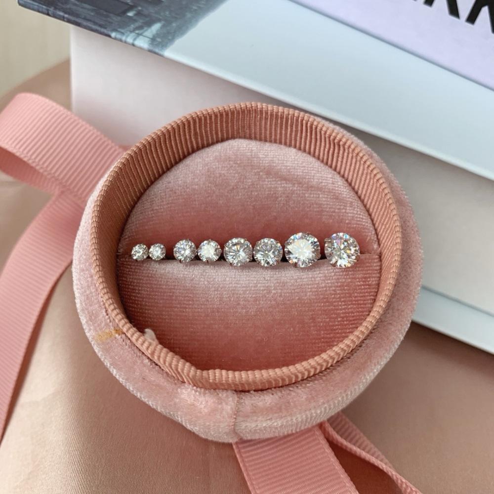 Multiple pairs of gold-plated barbell stud earrings featuring clear, faceted gemstones on a pink bag.