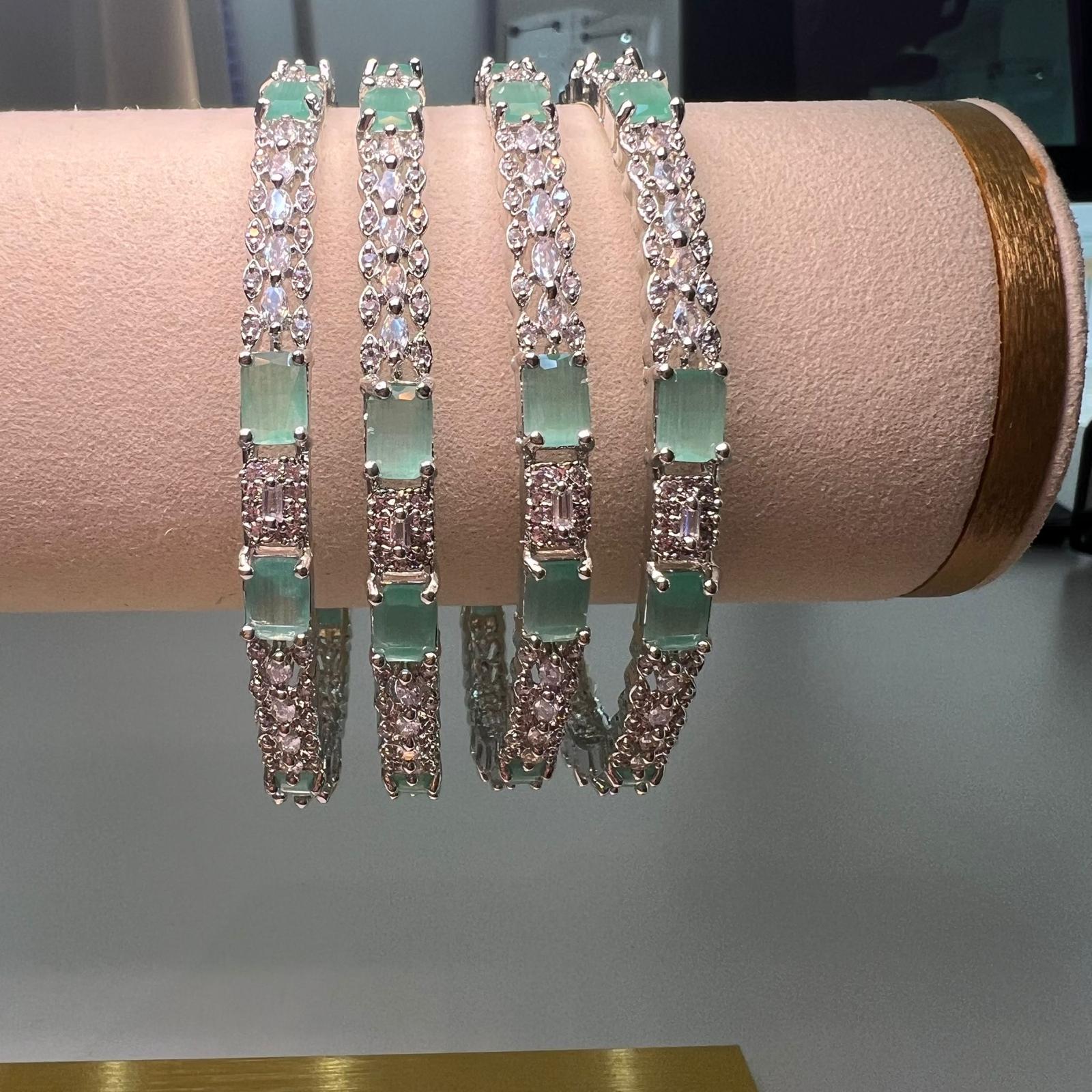 Set of silver bracelets with green stones on a pink cushion