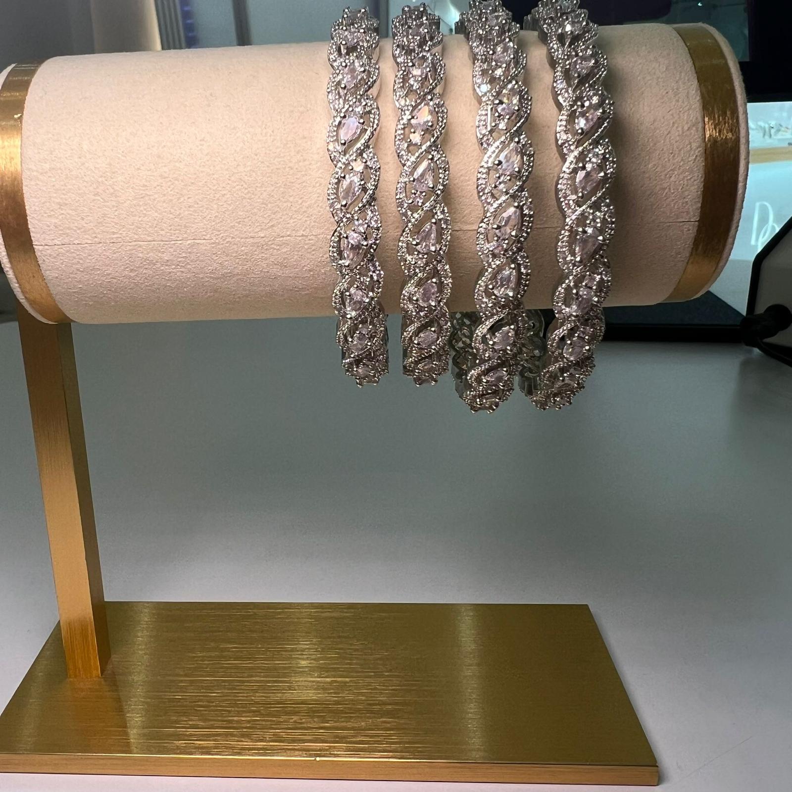 Set of silver bracelets on a gold stand with a white background
