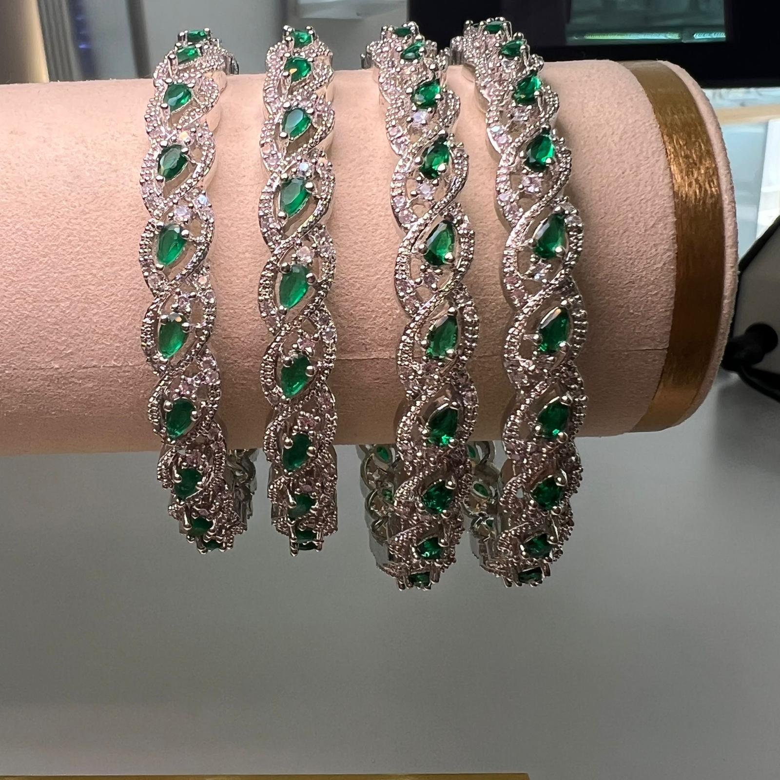 Four green gemstone bracelets on a pink cushion with a blurred background
