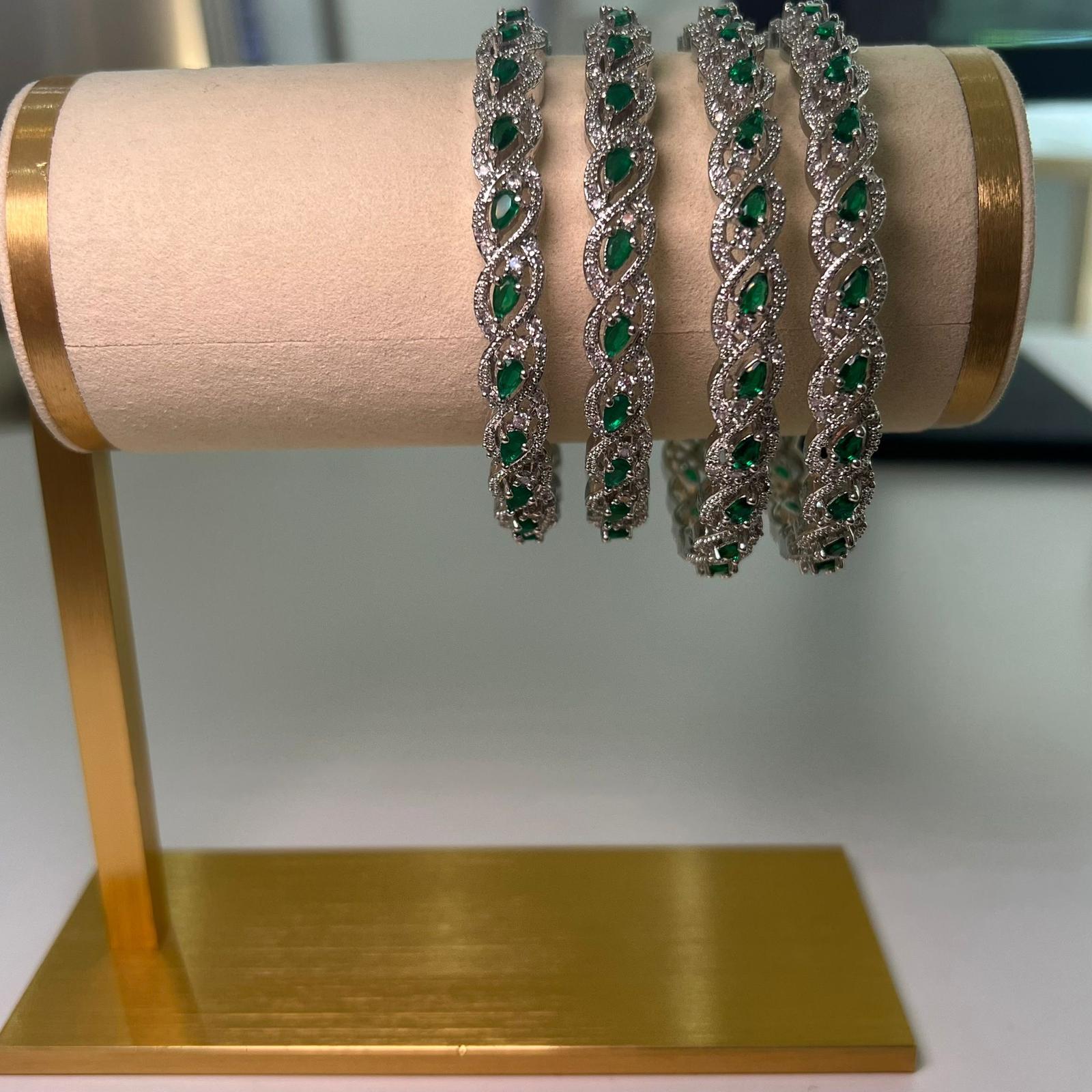 Four silver bracelets with green gemstones on a gold stand.