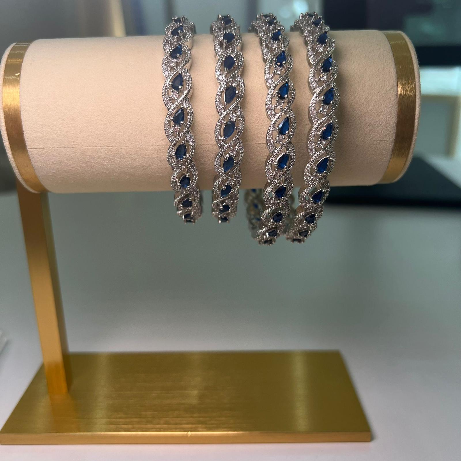 Four silver bracelets with blue stones on a gold stand.