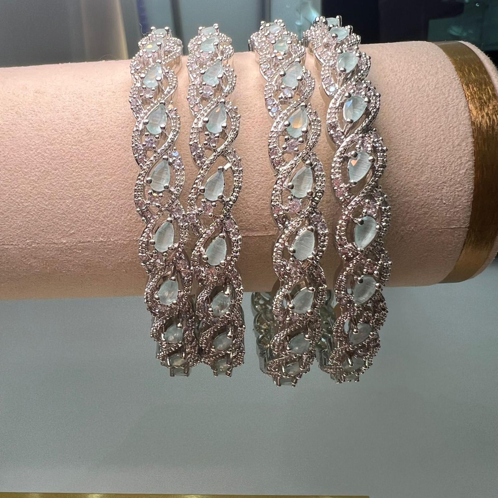 Four silver bracelets with light green gemstones on a pink stand.