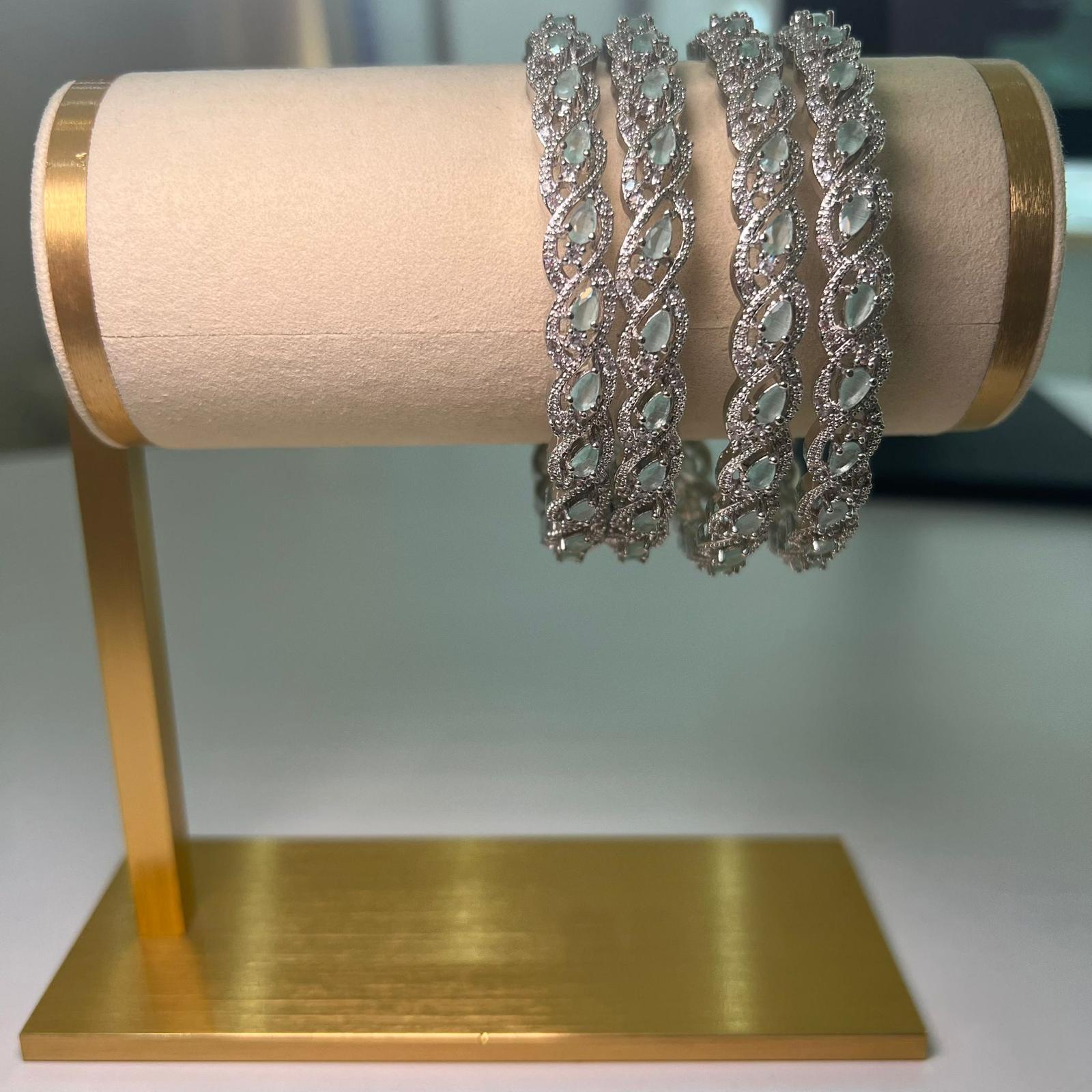 Four silver bracelets on a gold jewelry stand with a beige fabric background