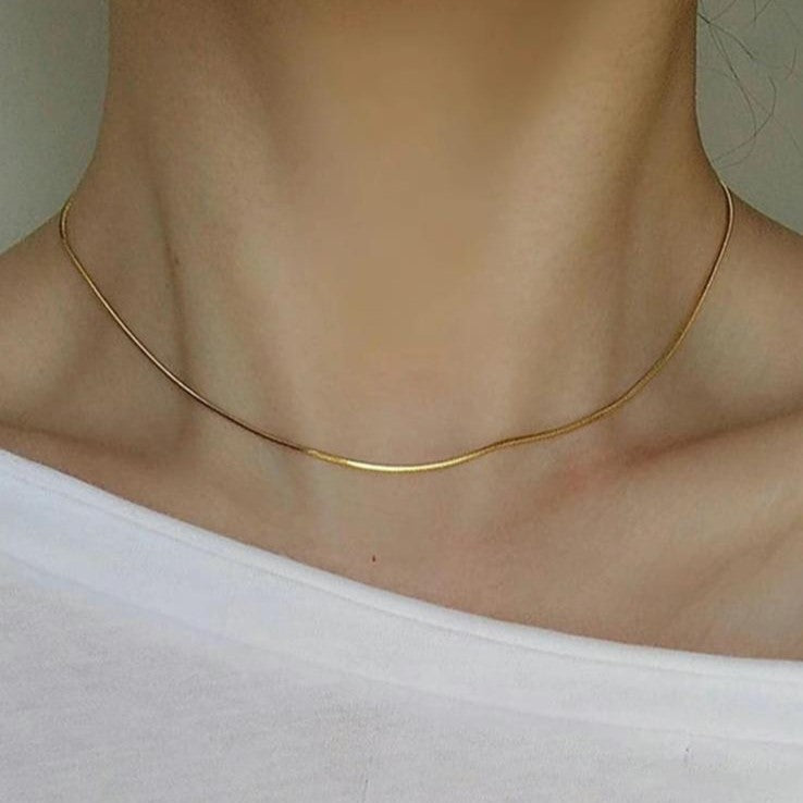 A sleek gold-colored stainless steel chain necklace displayed on a women's neck.