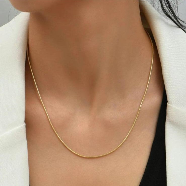 A sleek gold-colored stainless steel chain necklace displayed on a women's neck.