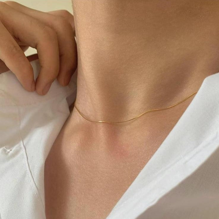 A sleek gold-colored stainless steel chain necklace displayed on a women's neck.