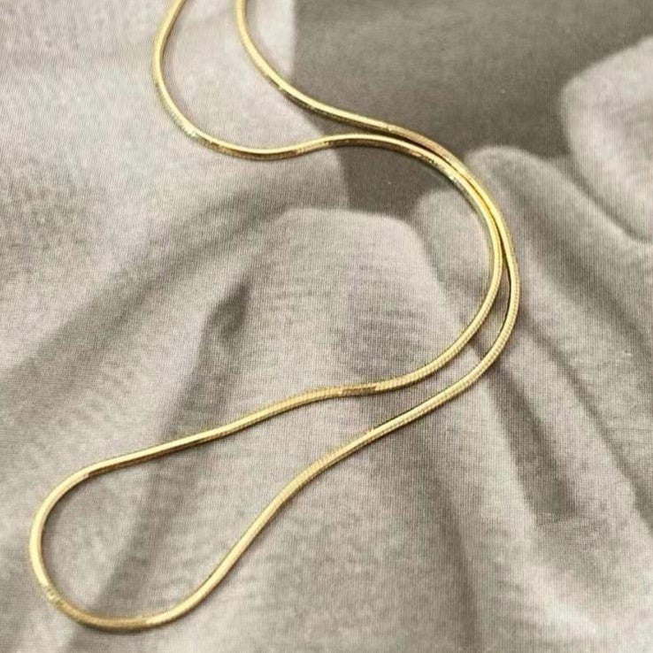 A sleek gold-colored stainless steel chain necklace displayed on a soft fabric.