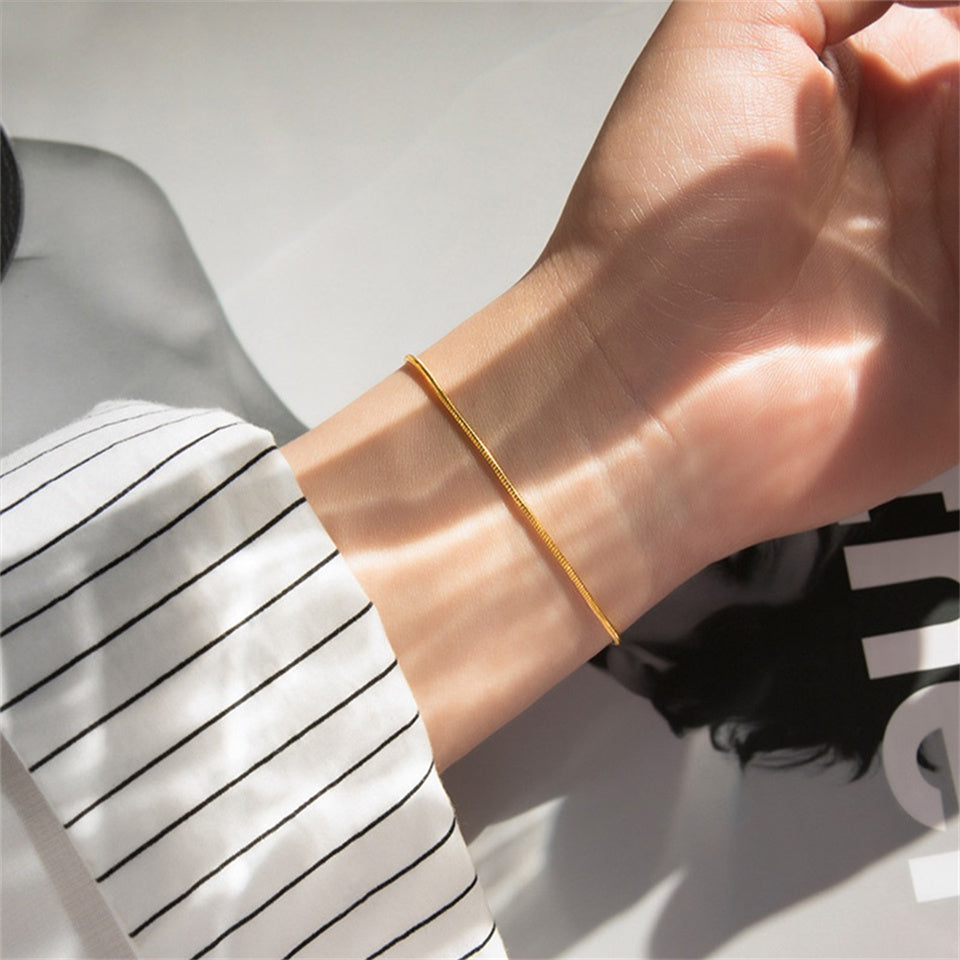 A gold-colored snake chain bracelet on a persons wrist.