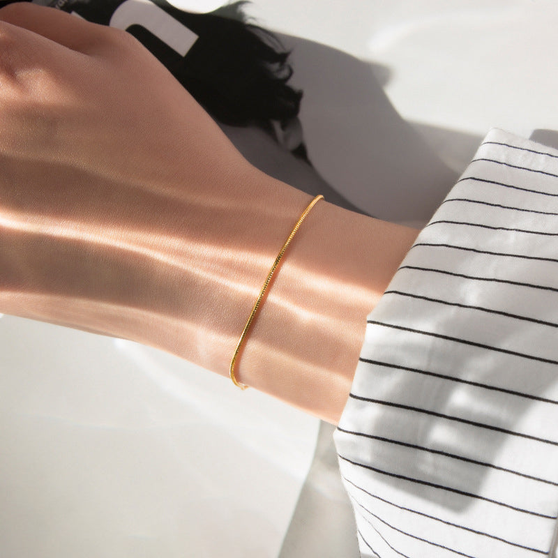 A gold-colored snake chain bracelet on a persons wrist.