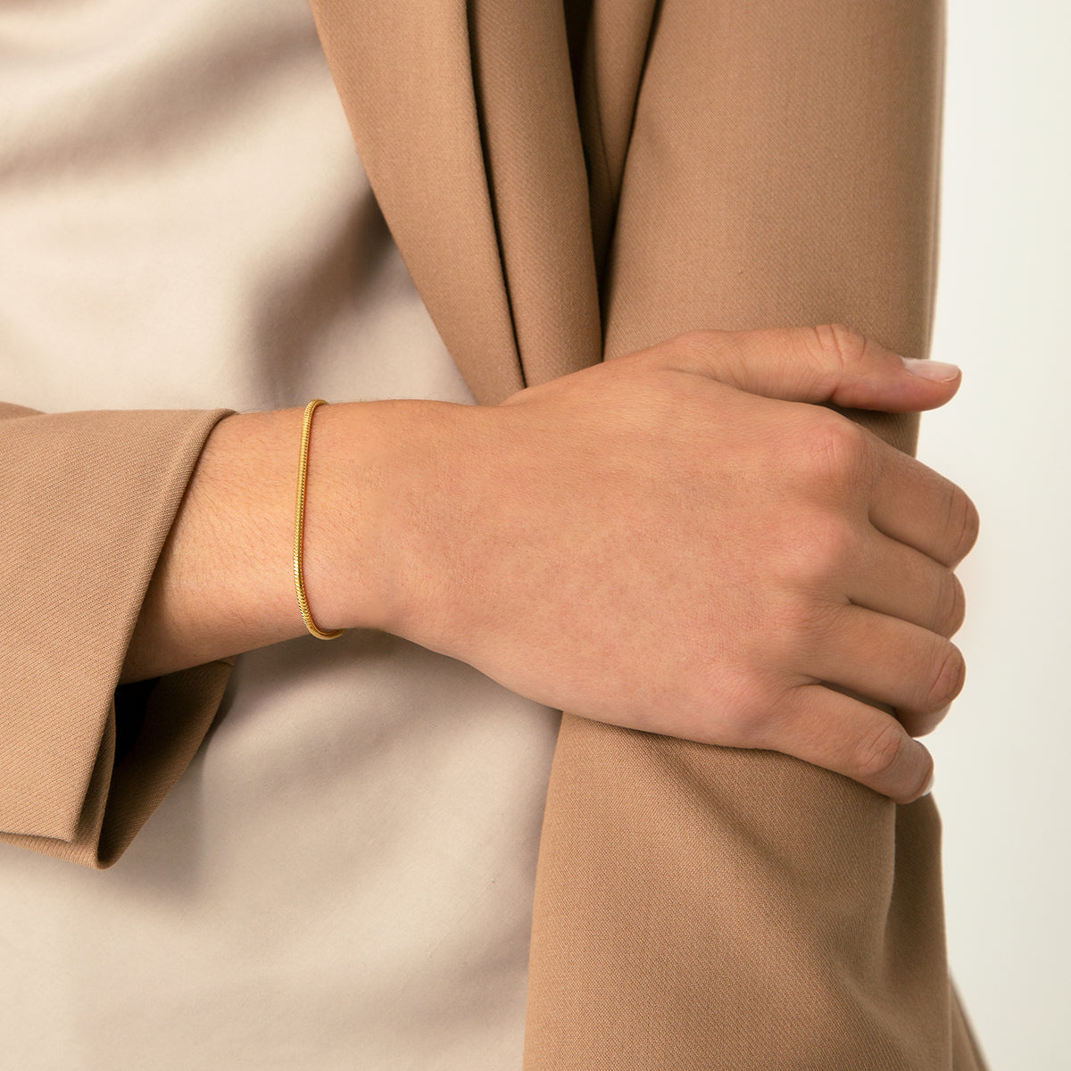 A gold-colored snake chain bracelet on a persons wrist.