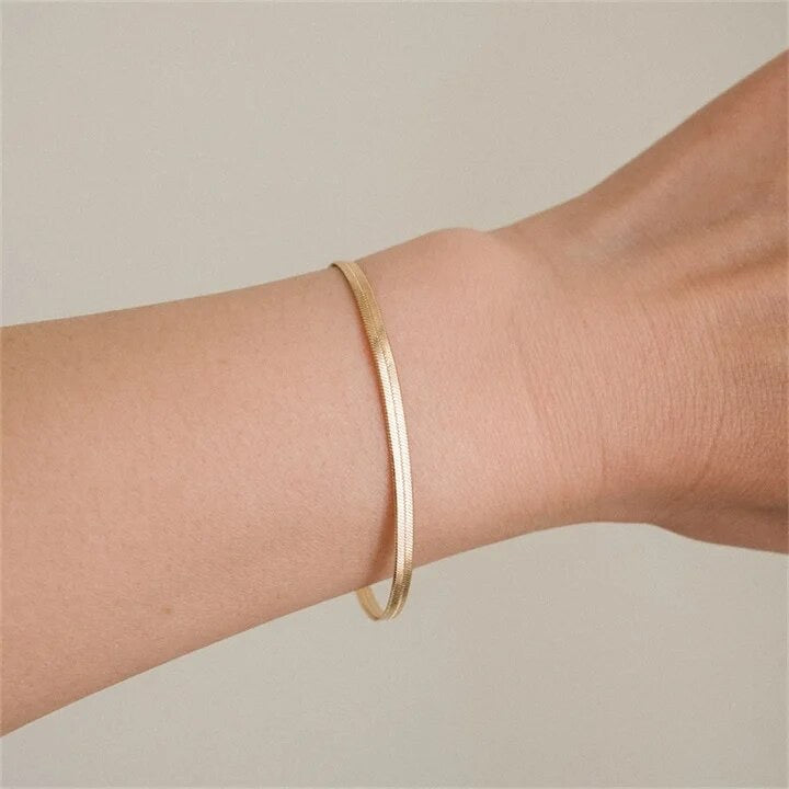 A gold-colored snake chain bracelet on a persons wrist.