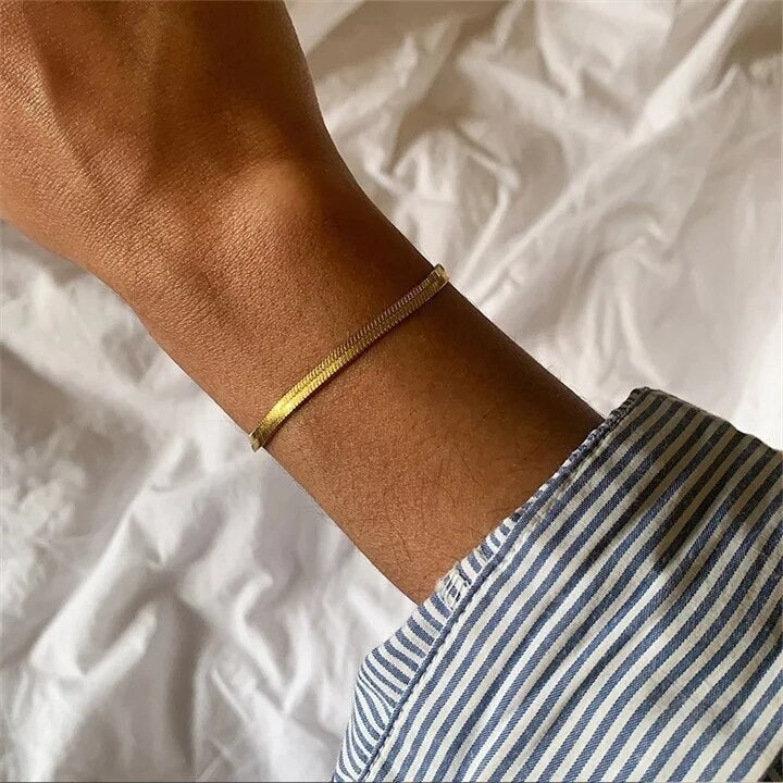 A gold-colored snake chain bracelet on a persons wrist.