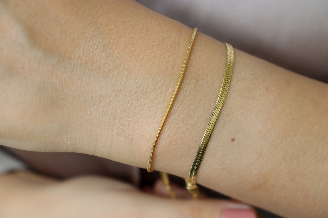 Two gold-colored snake chain bracelets on a persons wrist.