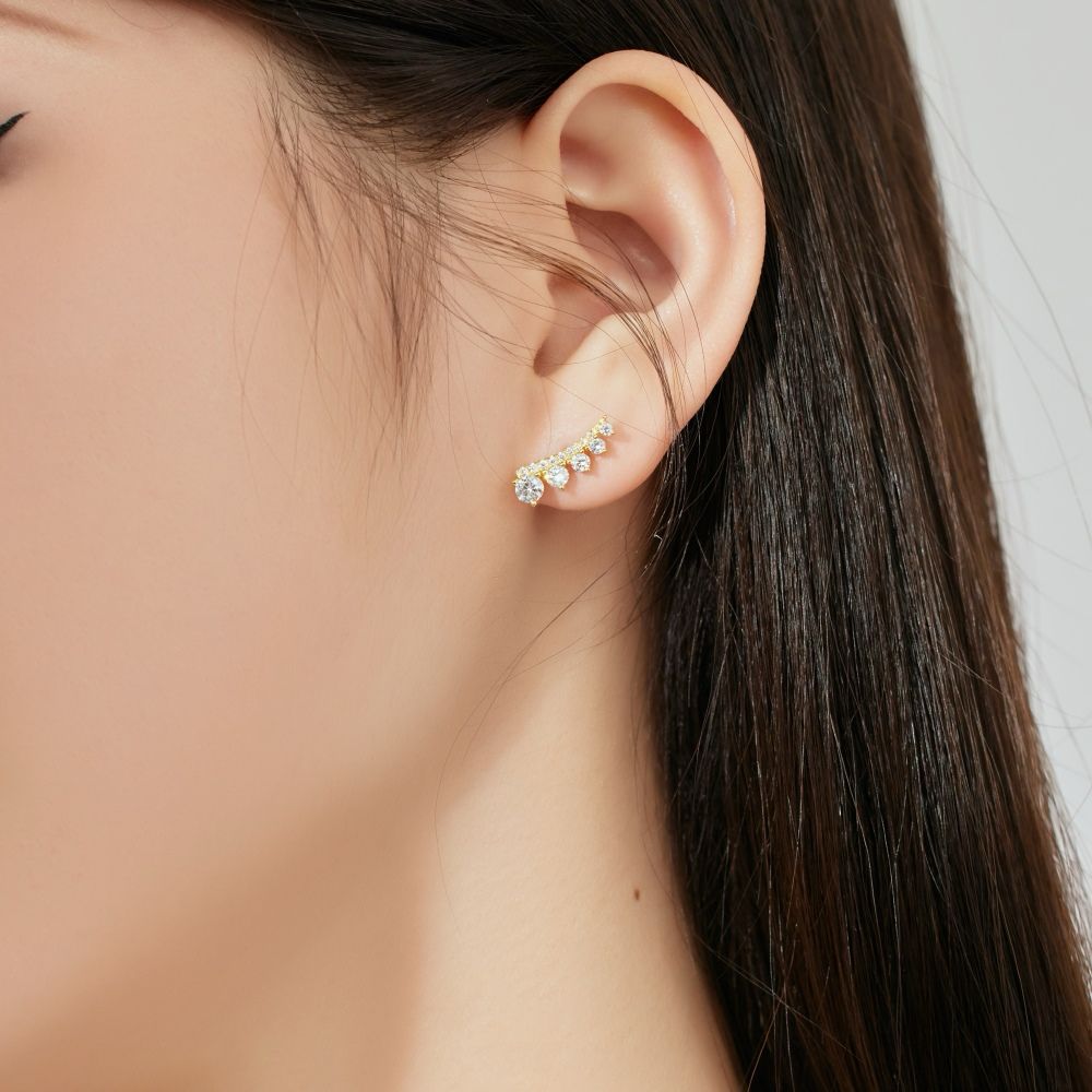 A gold-colored Stone Row earring featuring multiple round cut clear stones set in a row on a women's ear.