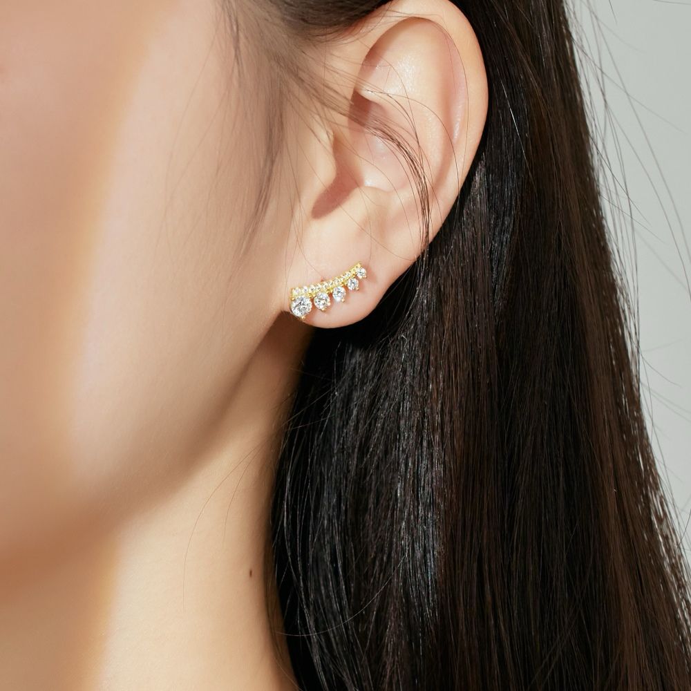 A gold-colored Stone Row earring featuring multiple round cut clear stones set in a row displayed on a women's ear.