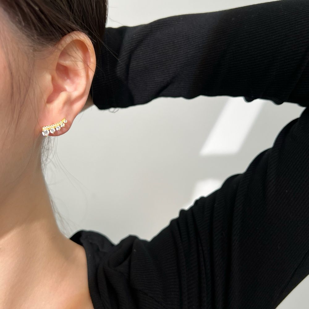 A gold-colored Stone Row earring featuring multiple round cut clear stones set in a row displayed on a women's ear.