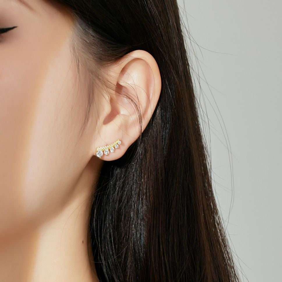 A gold-colored Stone Row earring featuring multiple round cut clear stones set in a row displayed on a women's ear.