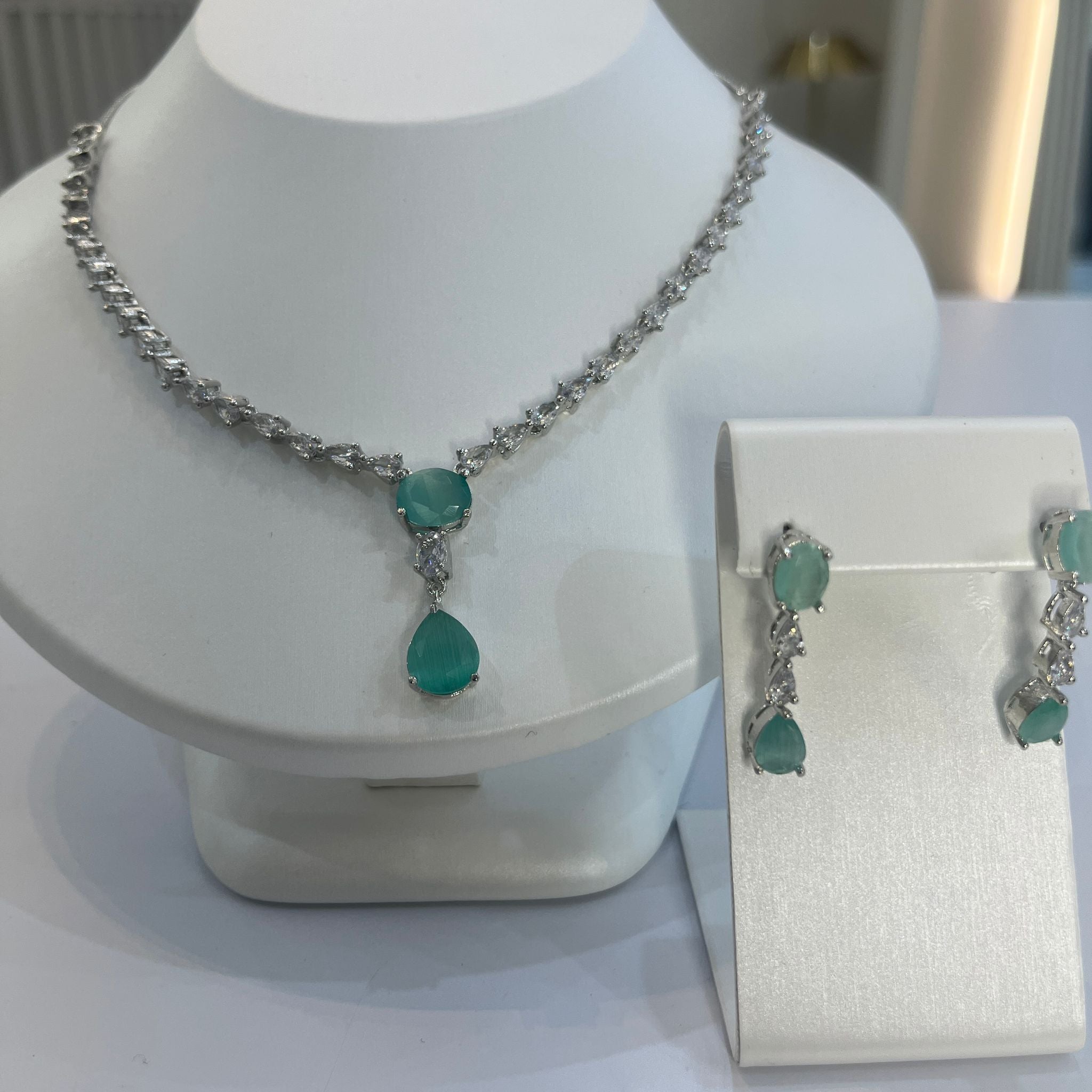 A teardrop necklace and earrings set displayed on a white mannequin. The set features a silver-tone chain with crystal embellishments and a teardrop pendant.