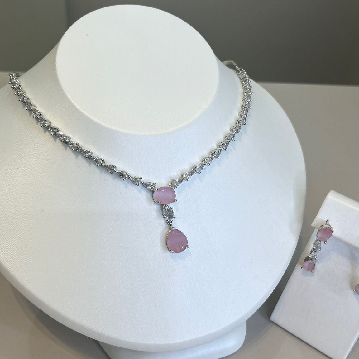 A teardrop necklace and earrings set displayed on a white mannequin. The set features a silver-tone chain with crystal embellishments and a teardrop pendant.