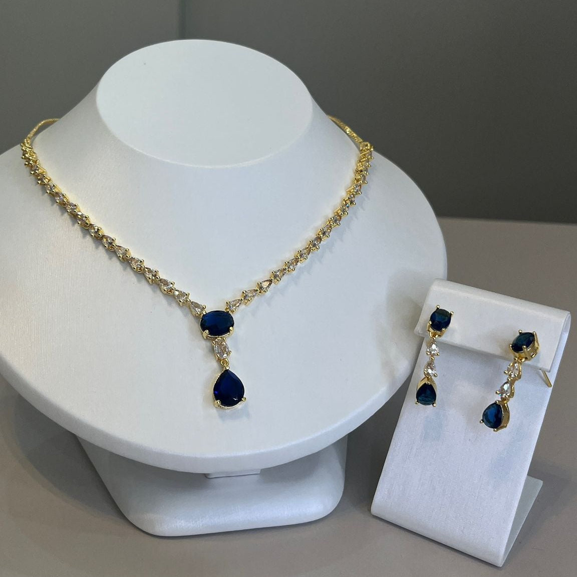 A teardrop necklace and earrings set displayed on a white mannequin. The set features a gold-tone chain with crystal embellishments and a teardrop pendant.