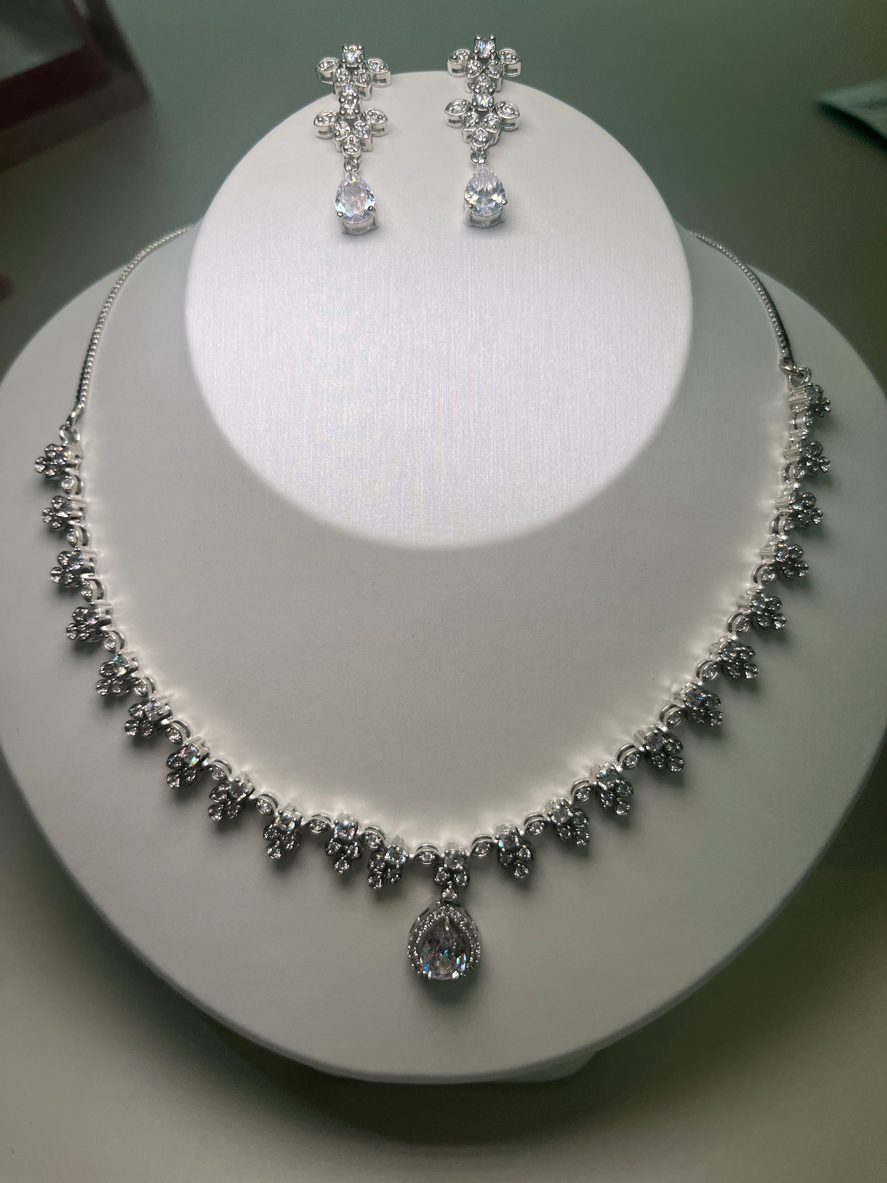 A necklace and earrings set featuring a teardrop-shaped gemstone centerpiece with a silver-tone finish, displayed on a mannequin bust.
