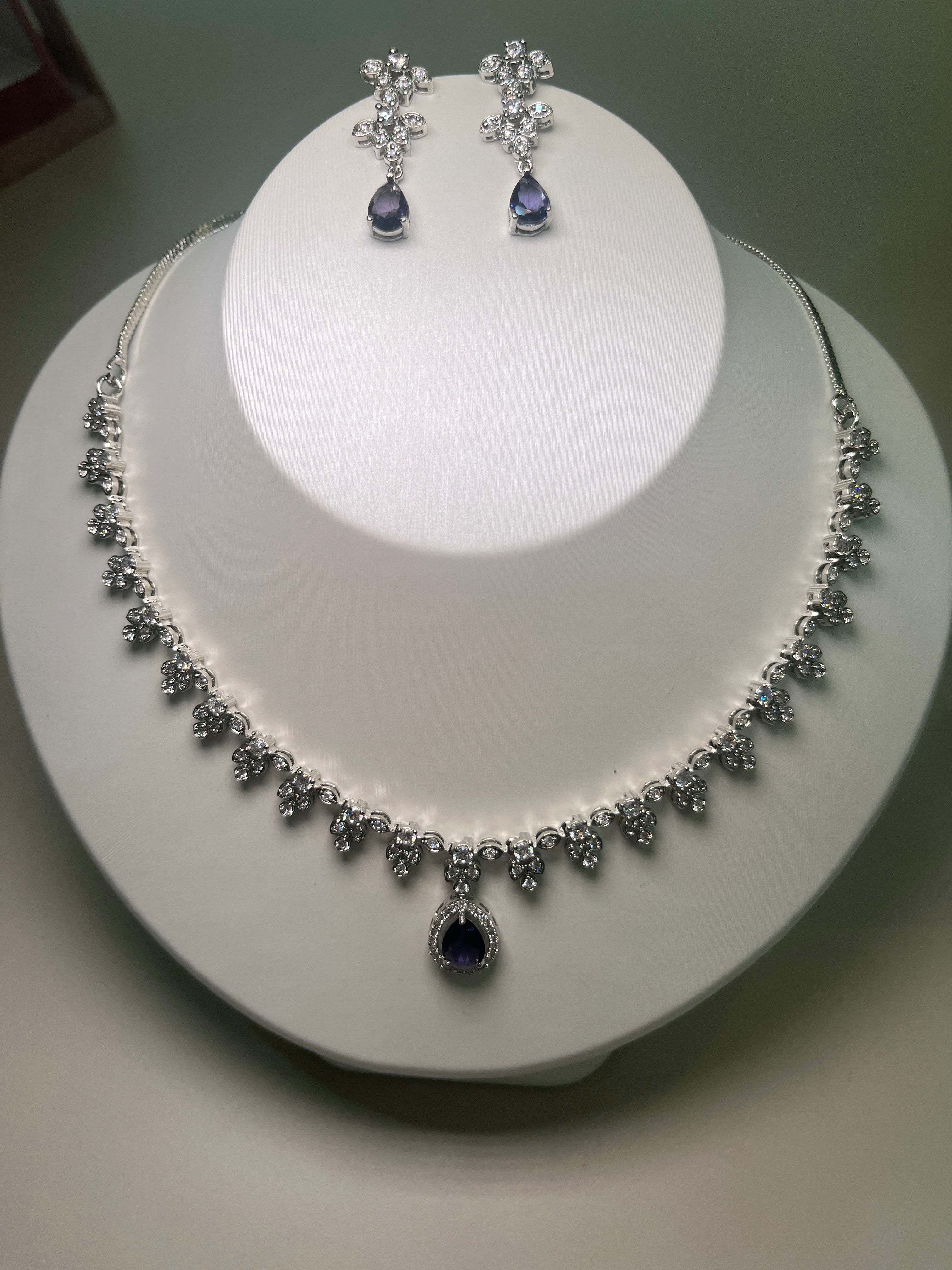 A necklace and earrings set featuring a teardrop-shaped gemstone centerpiece with a silver-tone finish, displayed on a mannequin bust.