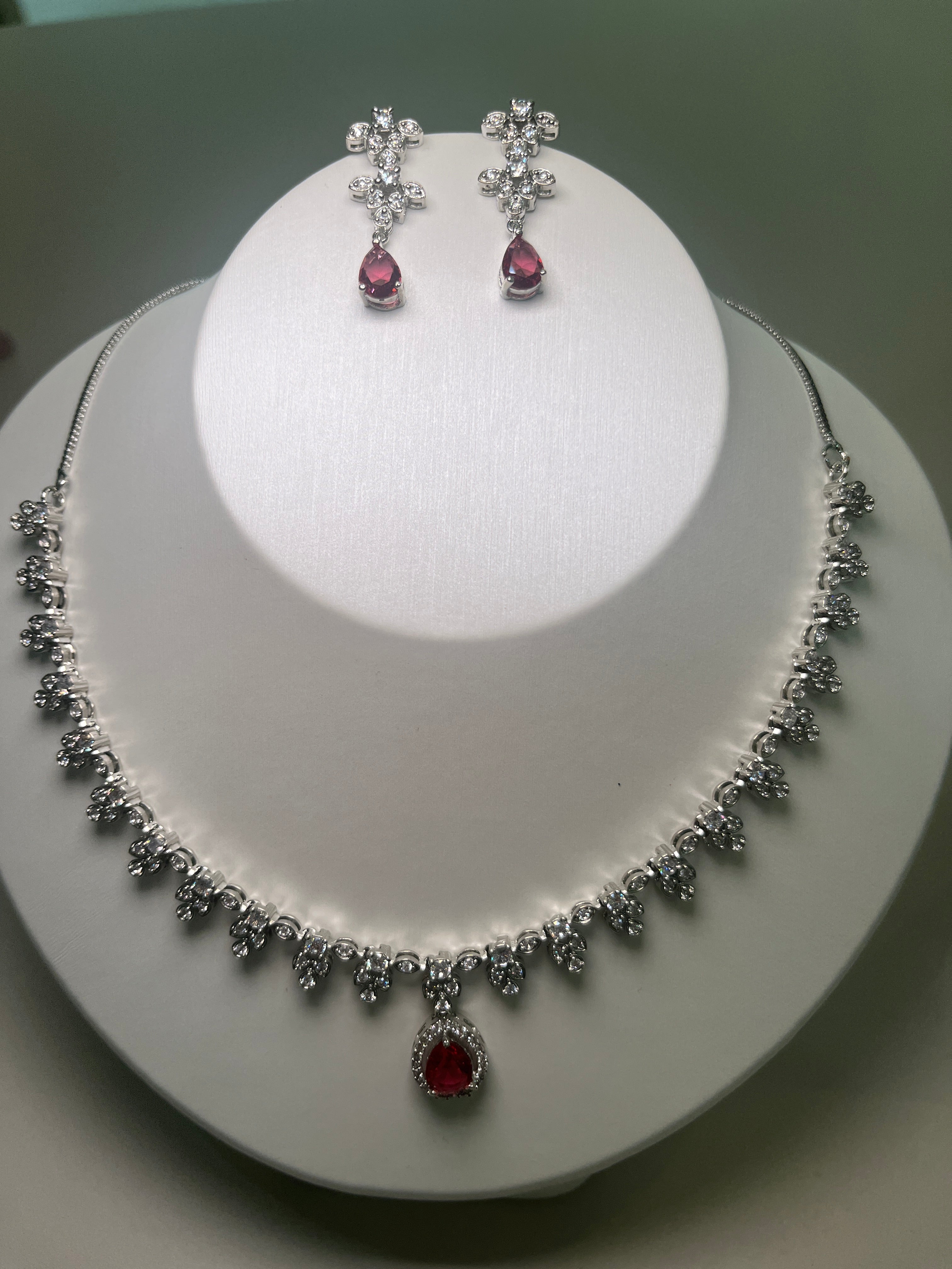 A necklace and earrings set featuring a teardrop-shaped gemstone centerpiece with a silver-tone finish, displayed on a mannequin bust.