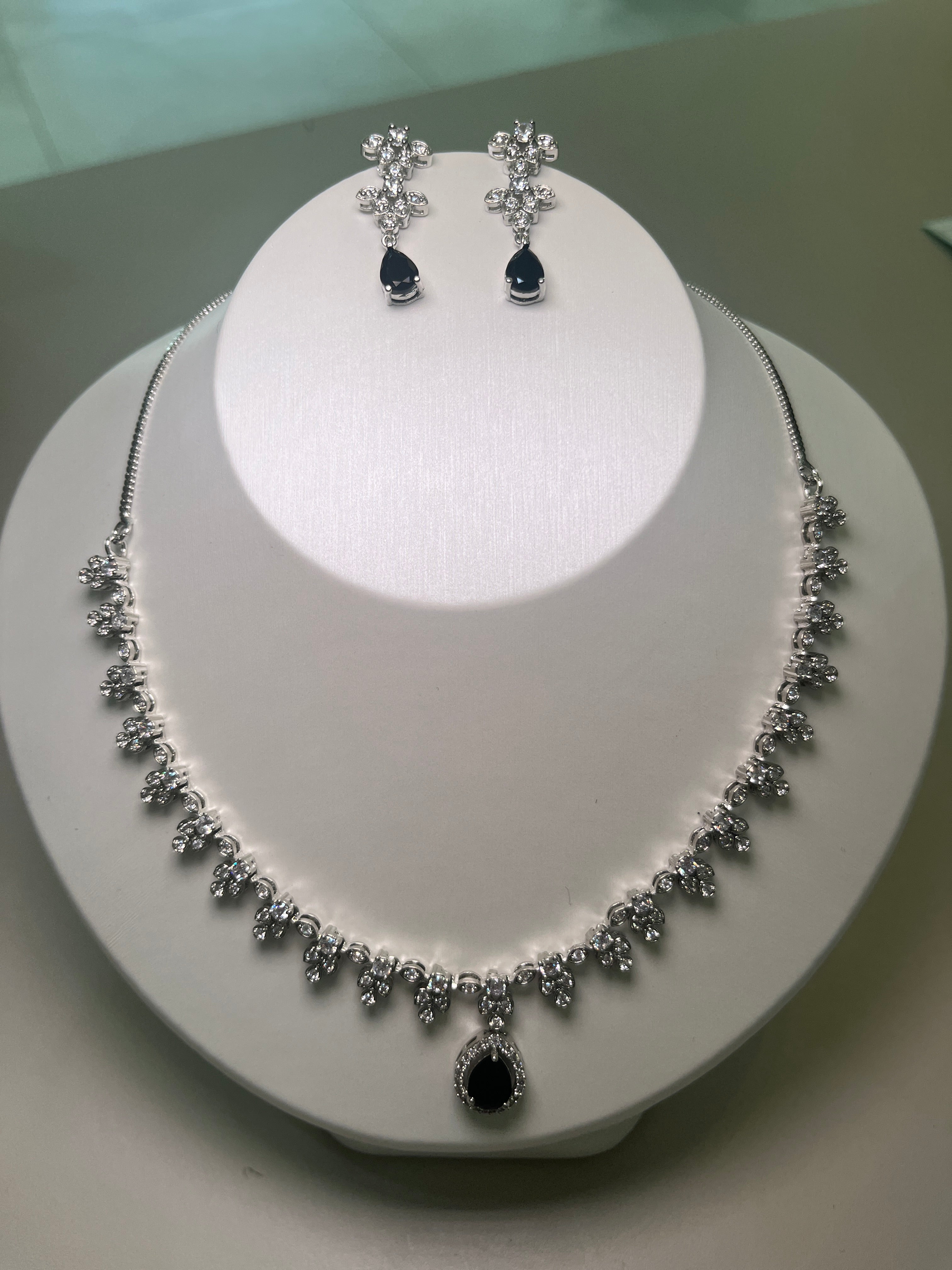 A necklace and earrings set featuring a teardrop-shaped gemstone centerpiece with a silver-tone finish, displayed on a mannequin bust.