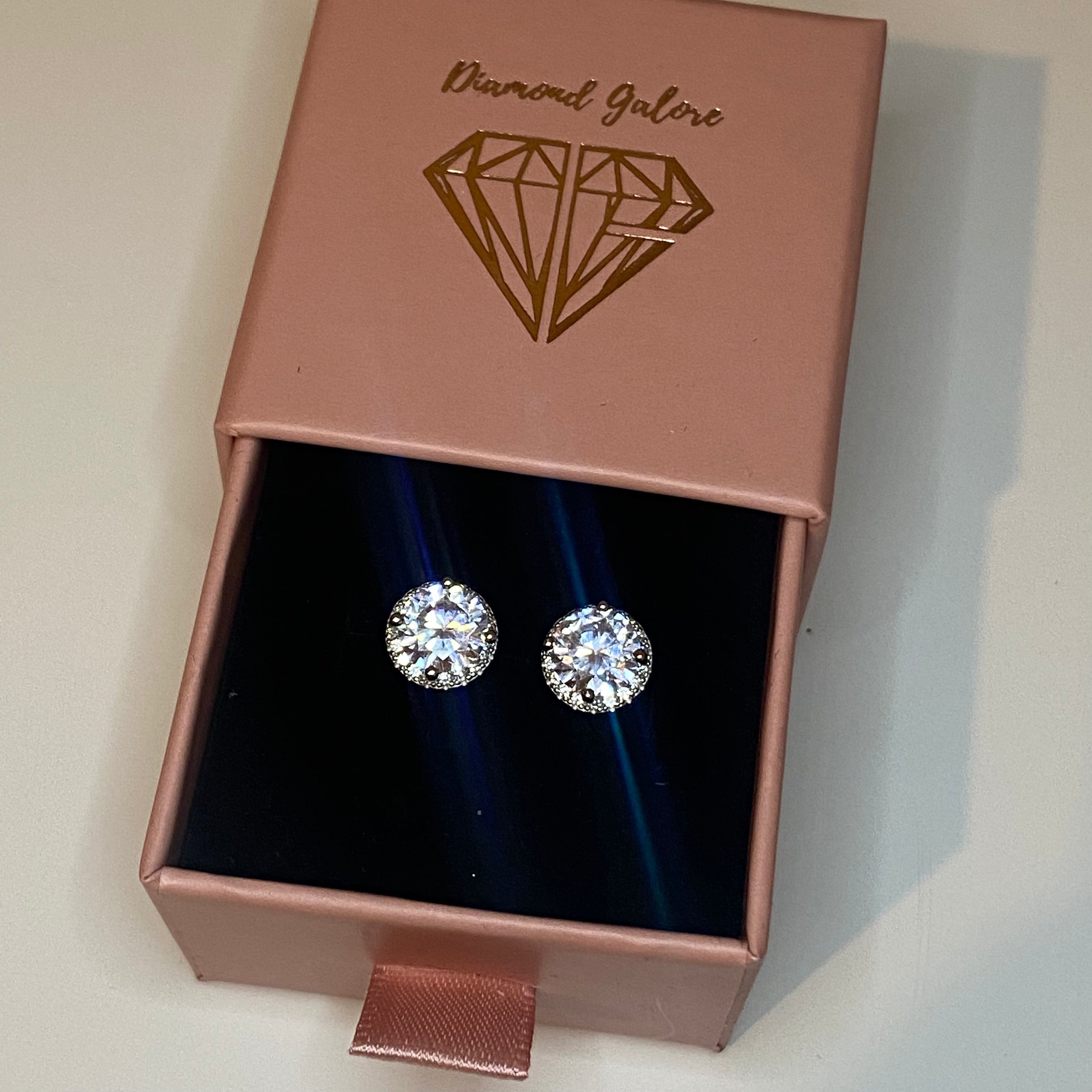 A pair of rhodium-plated stud earrings with a clear, zirconia main stone set in a small circle design.